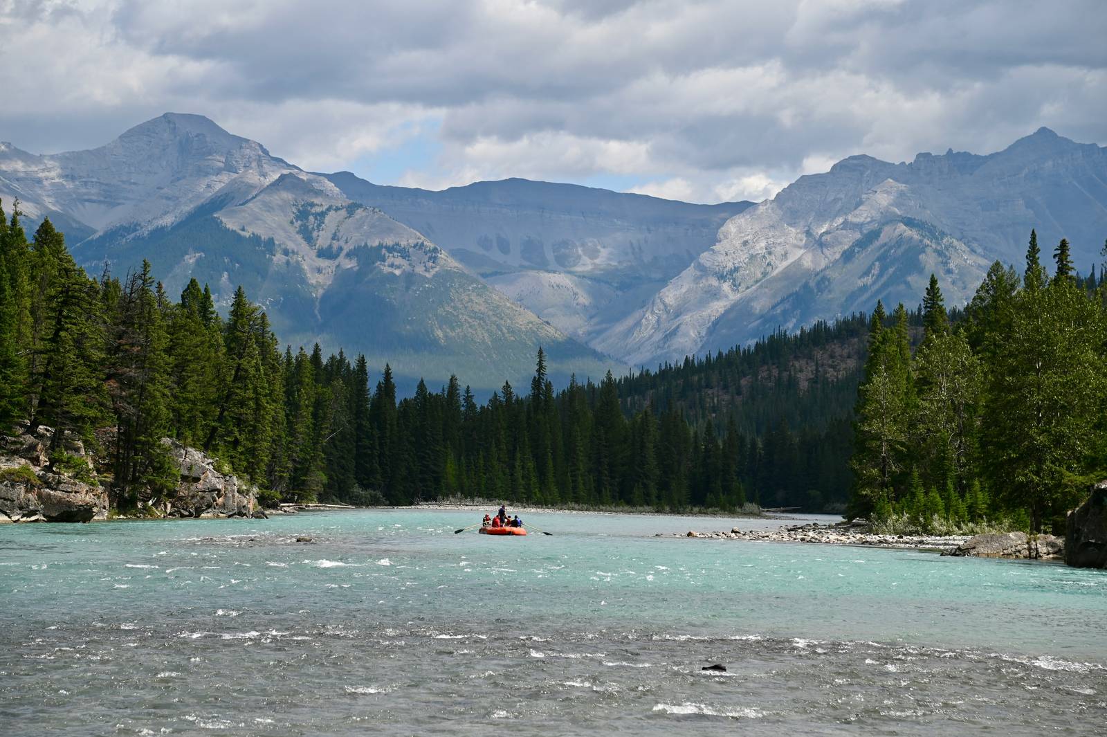 A raft on the turquoise Bow River in Banff National Park with mountains behind