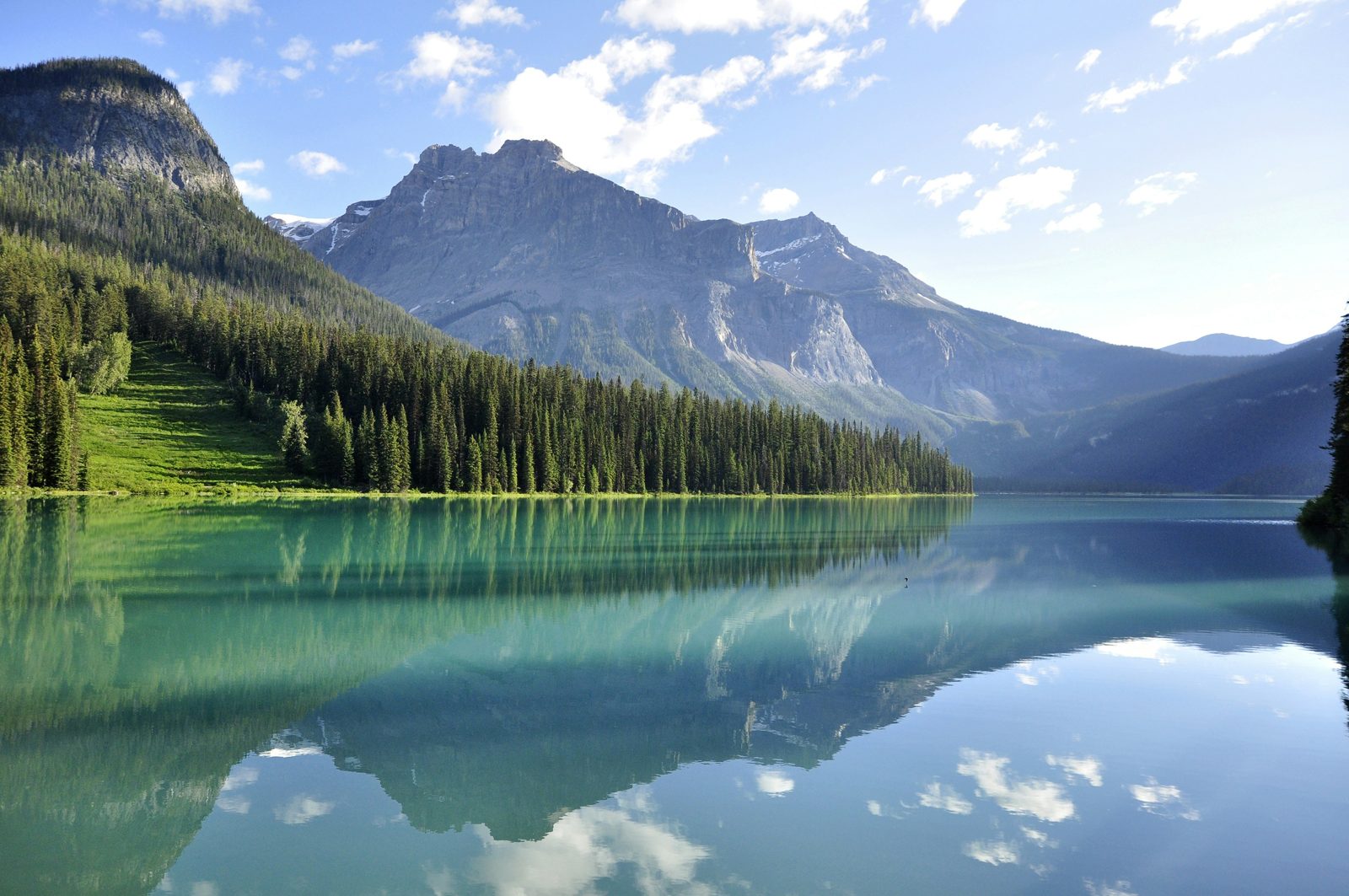 A still mountain lake reflecting forested slopes and rocky peaks in the Canadian Rockies