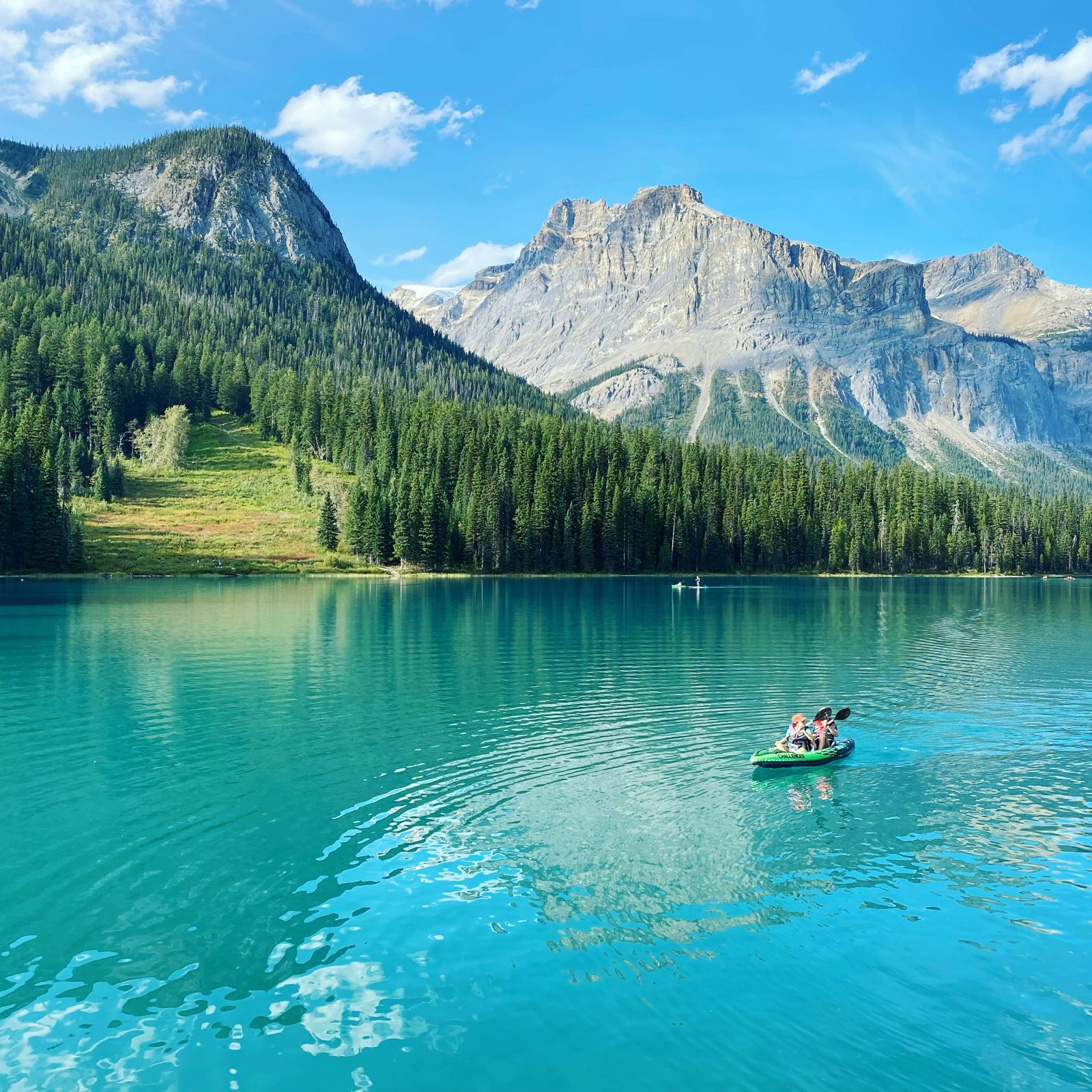 A canoeist on a turquoise mountain lake beneath forested slopes in Yoho National Park
