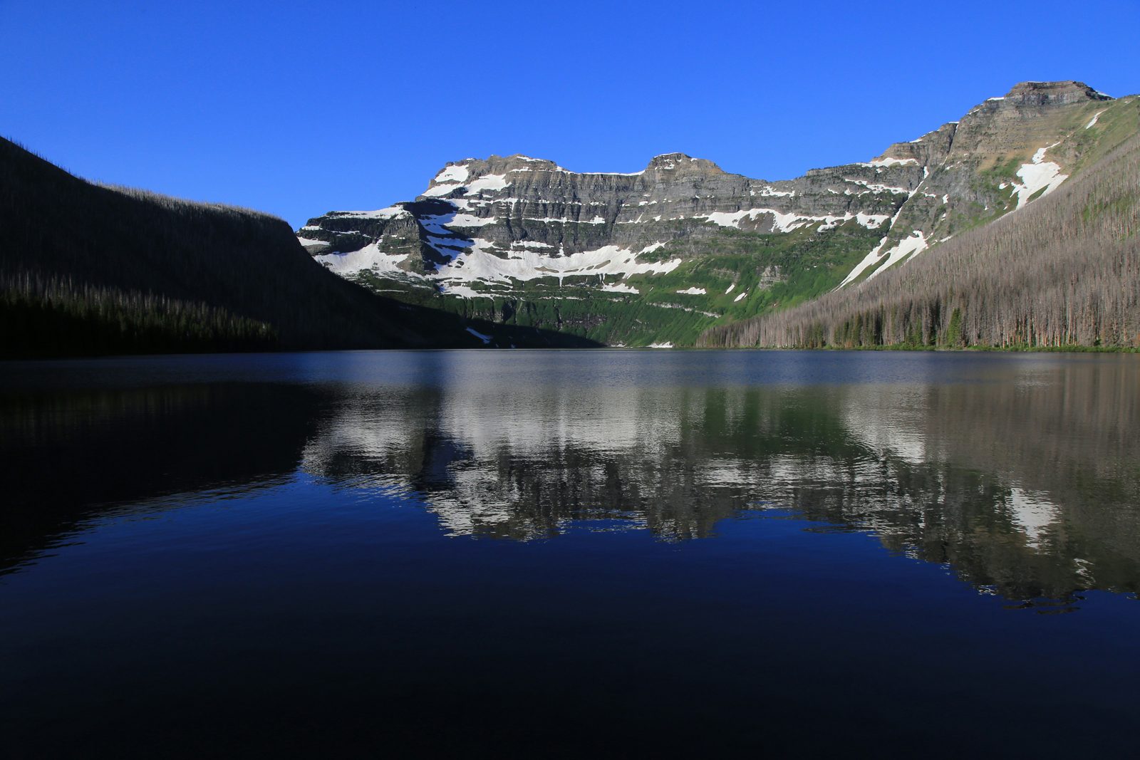 A calm mountain lake reflecting snow-patched peaks in Waterton Lakes National Park