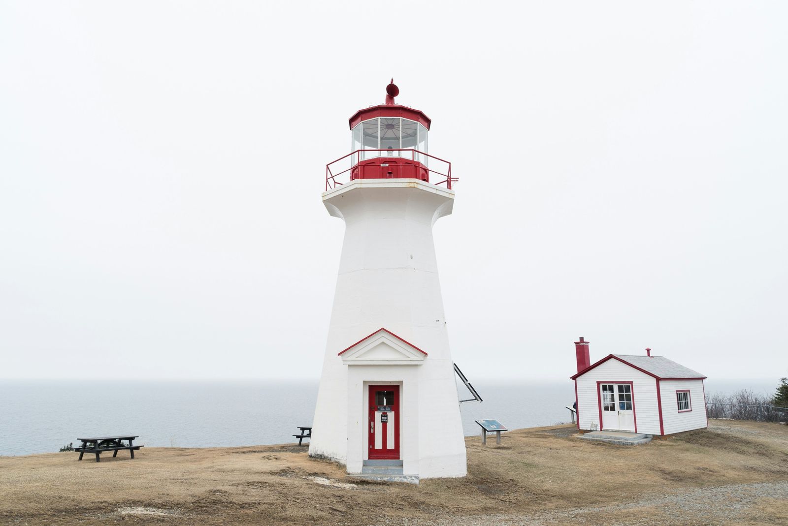 A white lighthouse with a red lantern and a small keeper’s building on a coastal headland