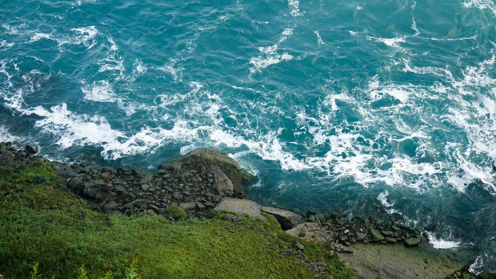 Turquoise water churning over rocks beside a grassy bank