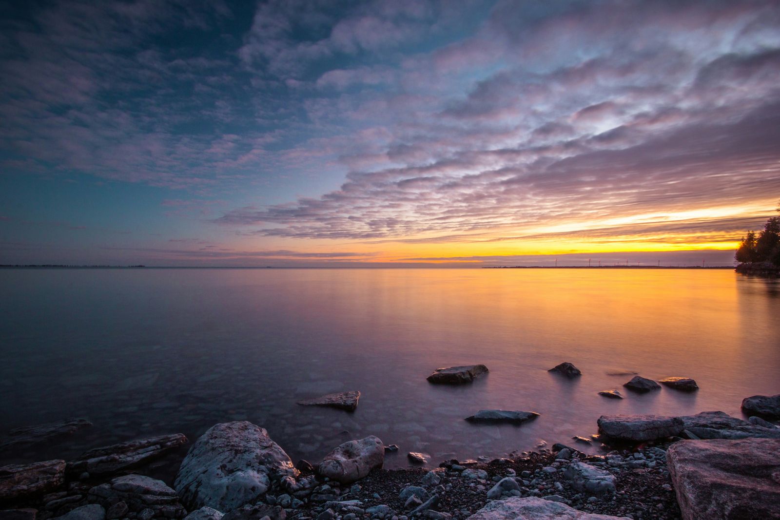 Sunset colours over a calm lake with rocks in the foreground