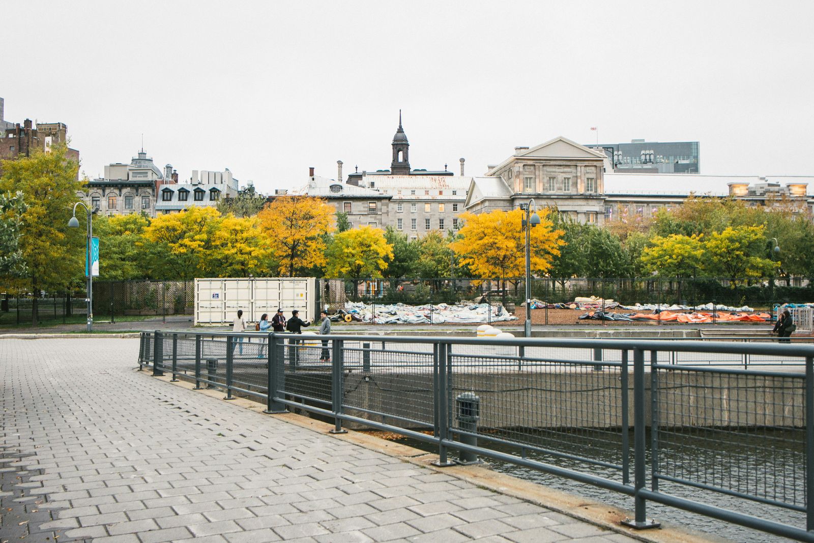 Autumn trees and heritage buildings behind a paved waterfront promenade in Old Montreal