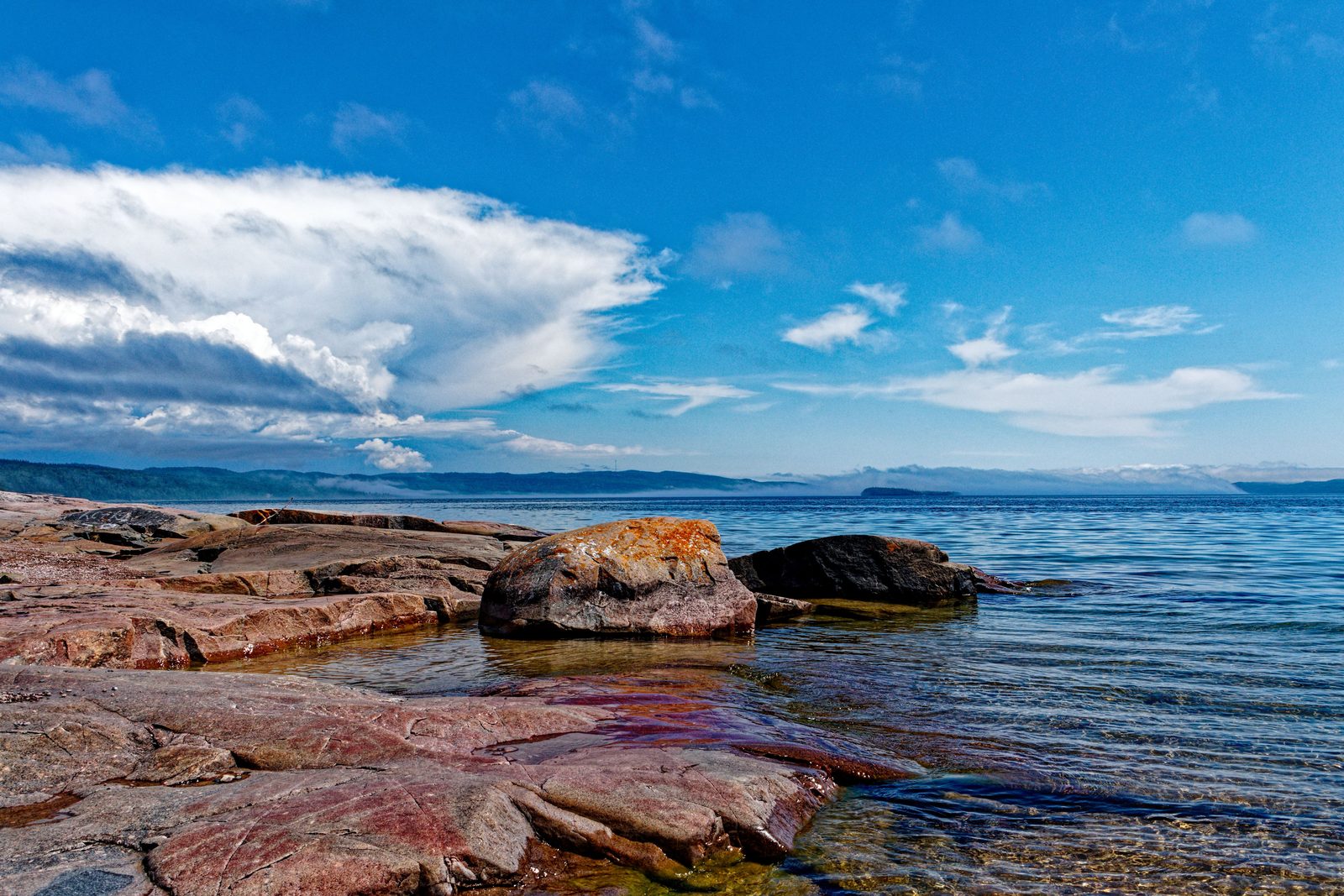 Smooth pink granite rocks along a Lake Superior shoreline under a blue sky