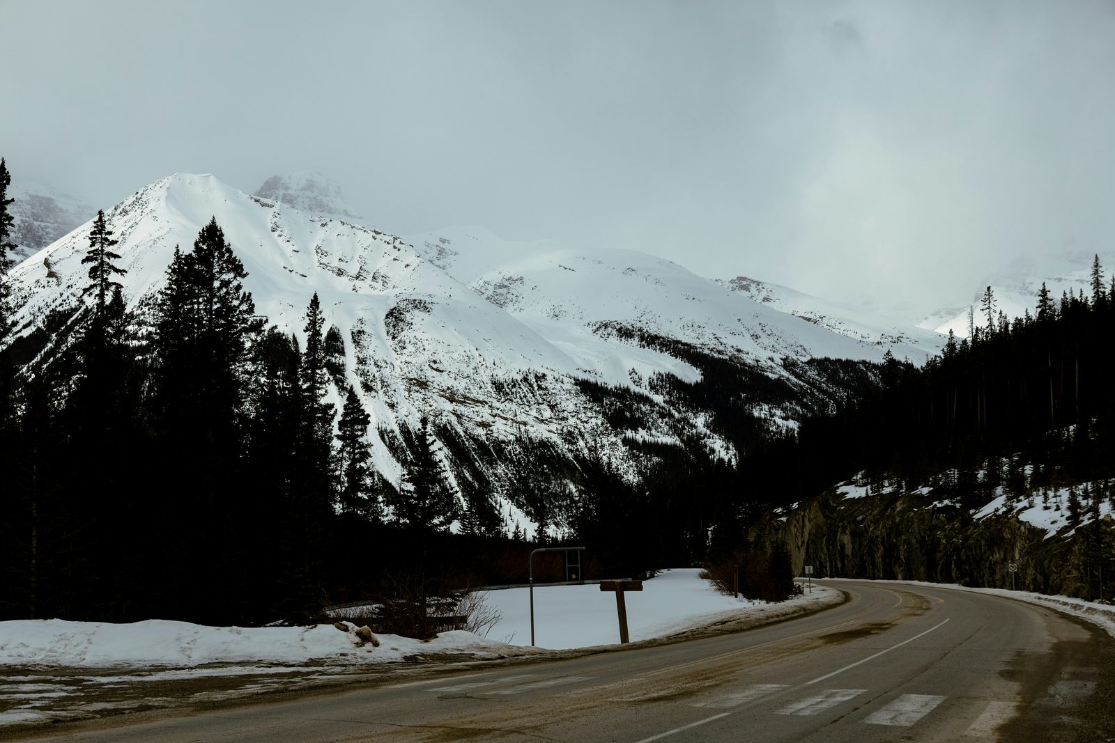 A curving mountain highway beside snow-covered peaks and dark forest