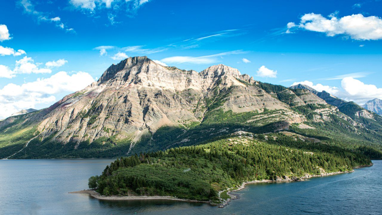 Forested peninsula and rugged mountain beside the deep blue water of Waterton Lakes National Park