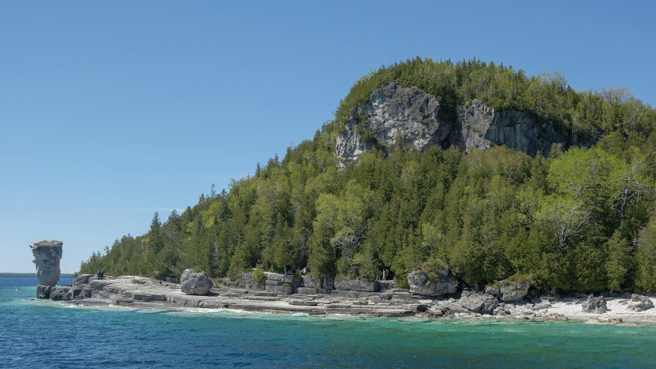 Flowerpot Island rock pillar beside a forested limestone cliff and turquoise Georgian Bay water